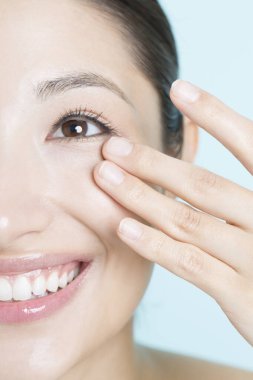 Genç Asyalı kadın yüzüne krem sürüyor. 