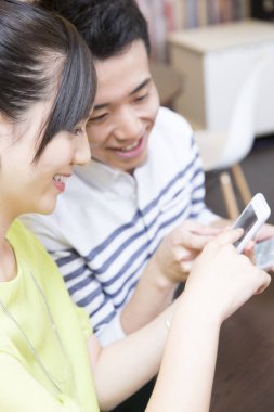 Ofiste akıllı telefon kullanan Asyalı genç ve neşeli bir çift.