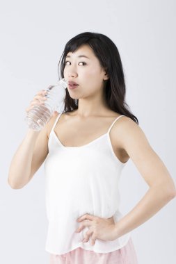 Genç Asyalı kadın şişeden su içiyor. 