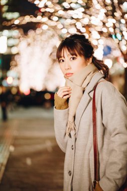 Sonbahar elbiseli güzel Japon kadın sokakta oturuyor, aydınlanmış şehir arka planında. 