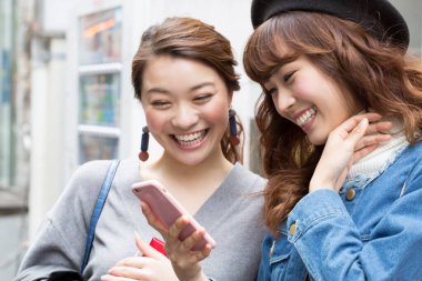 İki gülümseyen kadın cep telefonu kullanıyor.