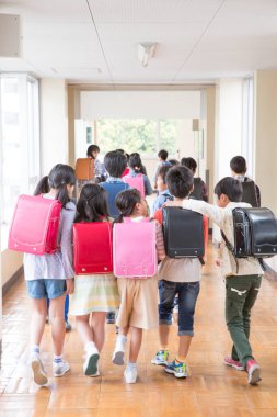 Okul koridorunda sırt çantalı bir grup Japon çocuk yürüyor. Arka plan