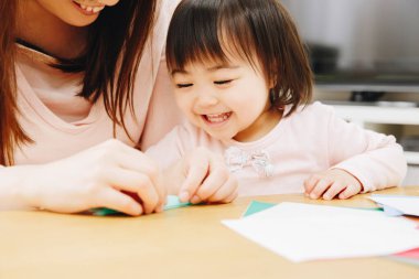 Annesi origami oyuncağı yapan küçük Asyalı çocuk. 