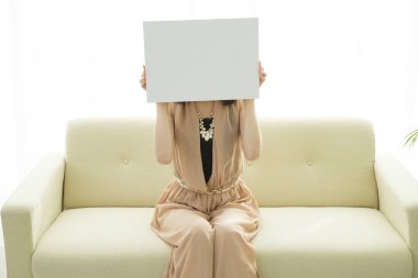 Genç bir kadın beyaz bir kanepede boş bir poster tutuyor.