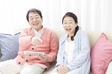 Kanepede televizyon izleyen Asyalı erkek ve kadının portresi.