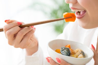 Genç Japon kadın çubuklarla yemek yiyor.