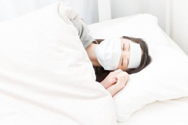 Maskeli hasta kadın beyaz yatakta uyuyor.