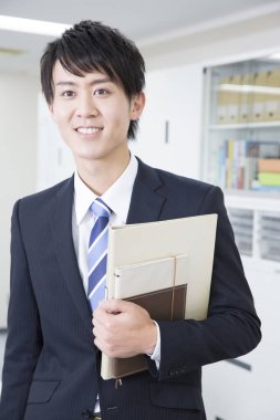 Ofiste elinde klasörlerle gülümseyen adam.