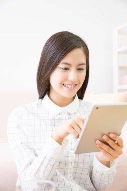 Genç Asyalı kadın evde dijital tablet kullanıyor.