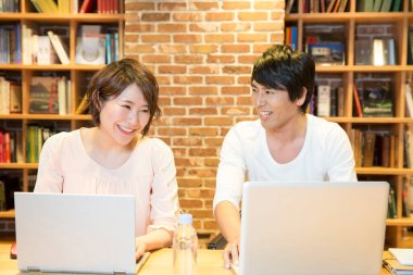 Genç Asyalı adam ve kadın kütüphanede çalışıyor.