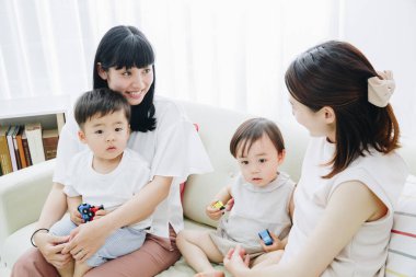 Neşeli Asyalı anneler ve çocuklar oturma odasında oynuyor.