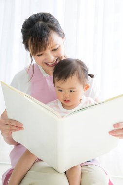 Asyalı anaokulu öğretmeni ve odada kitap okuyan sevimli küçük kız.