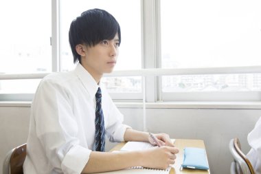 Genç adam sınıfın masasında çalışıyor.