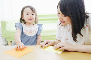 Anne ve kızı kağıtlarla oynuyor. 