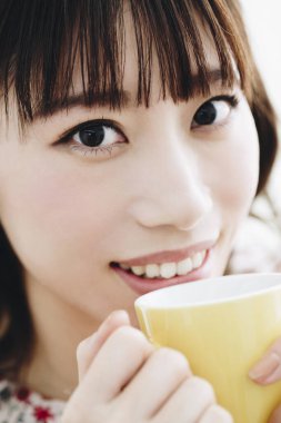 Genç Asyalı kadın odasında bir fincan kahve içiyor.