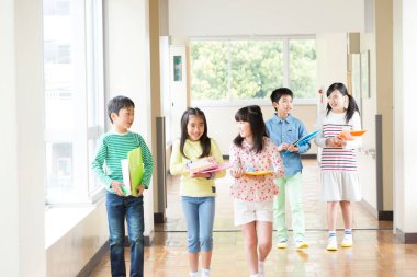 Okul koridorunda yürüyen kitaplarla bir grup Japon çocuk. 