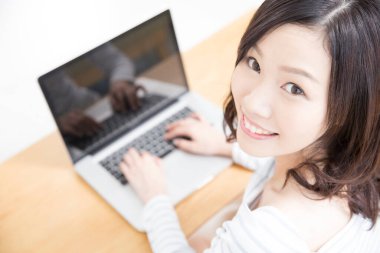 Evde dizüstü bilgisayar kullanan gülümseyen Asyalı kadın.