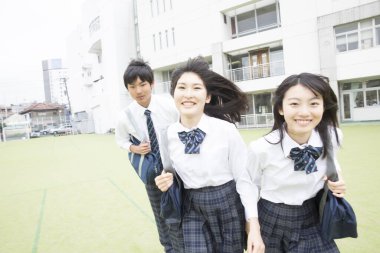 Dışarıda koşan öğrenciler okul üniformaları giyip gülümsüyor.