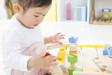 Tatlı Asyalı bebek çocuk odasında renkli tahta bloklarla oynuyor..