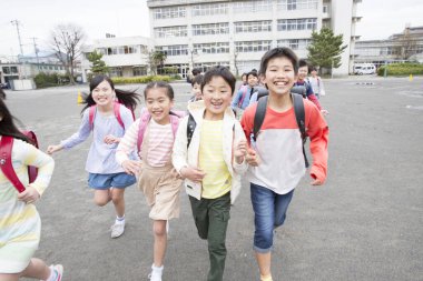 Okul bahçesinde koşan sırt çantalı bir grup Japon çocuk. 