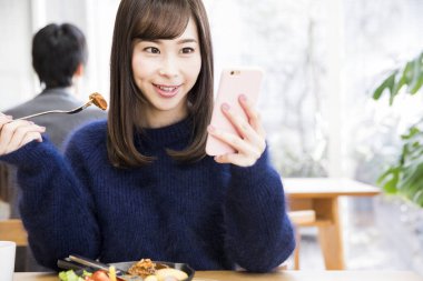 Japon restoranında yemek yerken akıllı telefon kullanan güzel genç bir kadın. 