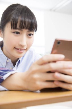 Asyalı kadın evde akıllı telefon kullanıyor.