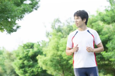 Genç yakışıklı Asyalı adam parkta koşuyor. 