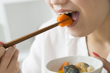 Asyalı kadın evde çubuklarla yemek yiyor.