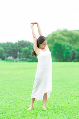 Yeşil yaz parkında elini uzatan beyaz elbiseli genç Japon kadın.