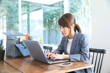 Ceketli Asyalı genç kadın ofisinde dizüstü bilgisayarla çalışıyor. 