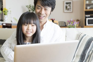 Evde dizüstü bilgisayar kullanan mutlu bir Asyalı aile.