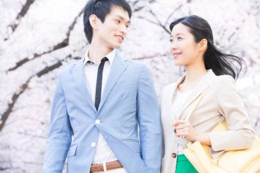 Parkta çiçek açan sakura ağaçları olan genç Asyalı çift.