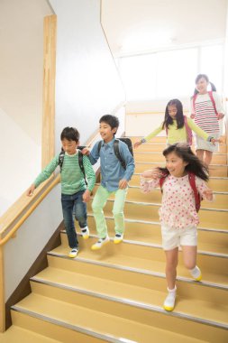 Çocuklar okulda merdivenlerde koşuyor. 