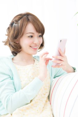 Genç Asyalı gülümseyen kadın akıllı telefon kullanıyor.