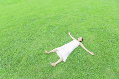 Beyaz elbiseli güzel Japon kadın yaz parkında yeşil çimlerin üzerinde yatıyor.