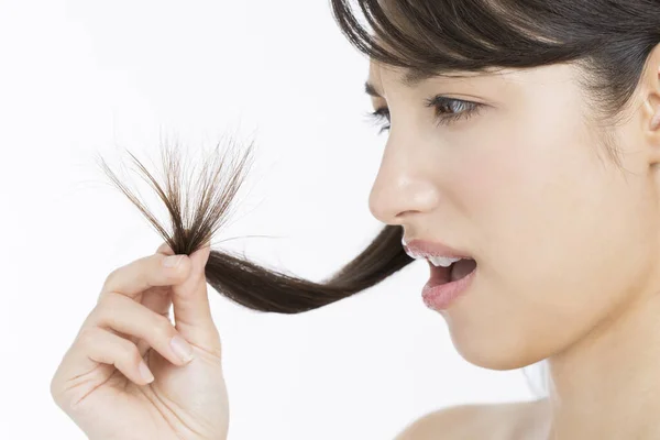 アジアの女性は彼女の長い髪を保持し 髪の毛の破損した分割端を見ています — ストック写真