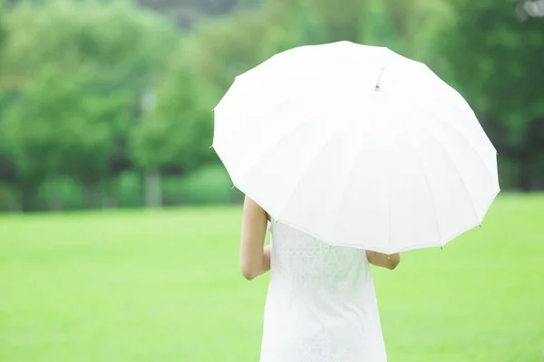 緑の夏の公園を歩いている白い傘を持つ若い日本人女性 白いドレスで若い女性の昼間の肖像画 — ストック写真