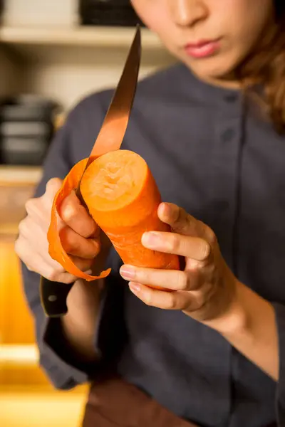 年轻的亚裔女服务员在厨房剥去胡萝卜皮 — 图库照片