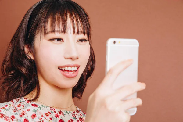 Genç Asyalı kadın cep telefonuyla selfie çekiyor.
