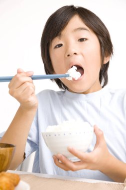 Asyalı küçük çocuk, beyaz arka planda izole edilmiş çubuklarla pirinç yiyor.