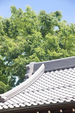Arka planda yeşil ağaçlar olan Japon tapınağının çatısı.