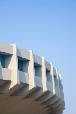 Mavi gökyüzüne karşı geometrik şekiller içeren modern beton bina dış yüzeyi