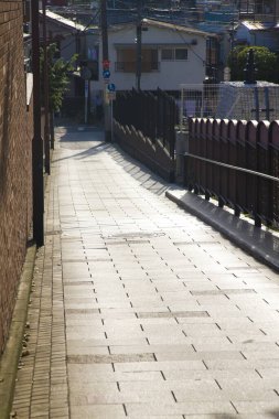 Güneş ışığı konut binalarının yanındaki boş dar kaldırımlı sokağı aydınlatıyor.