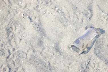 Çöpe atılmış plastik şişe kumlu sahil yüzeyinde dinleniyor.