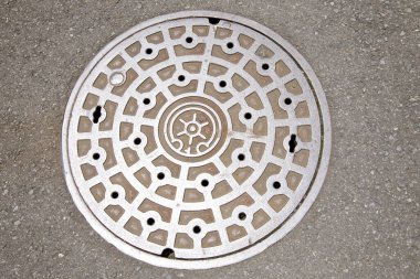 Beton kaldırım yüzeyinde duran yuvarlak metal rögar kapağı