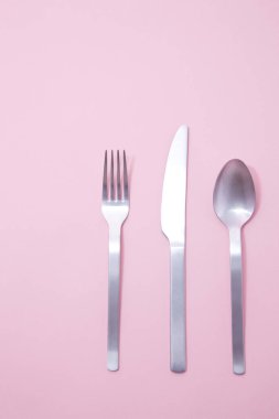 Pembe arka planda metal çatal bıçak takımı.