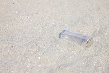 Çöpe atılmış plastik şişe kumlu sahil yüzeyinde yatıyor.
