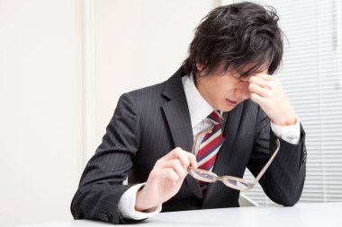 Masada oturan, başı ağrıyan Asyalı adam. 