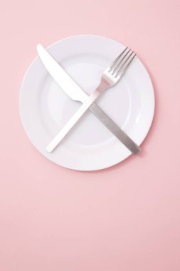 Çapraz çatallı boş tabak ve pembe arka planda bıçak, üst manzara.