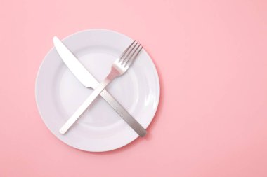 Pembe arka planda çapraz çatal bıçak takımı olan beyaz tabak
